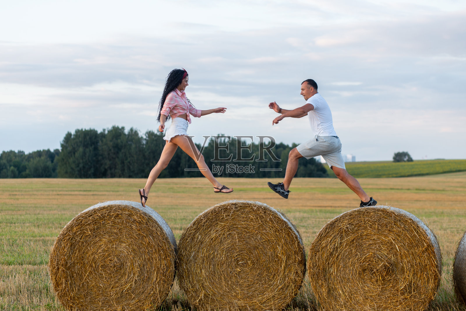 一对恩爱的夫妇在田野里的稻草卷上。照片摄影图片
