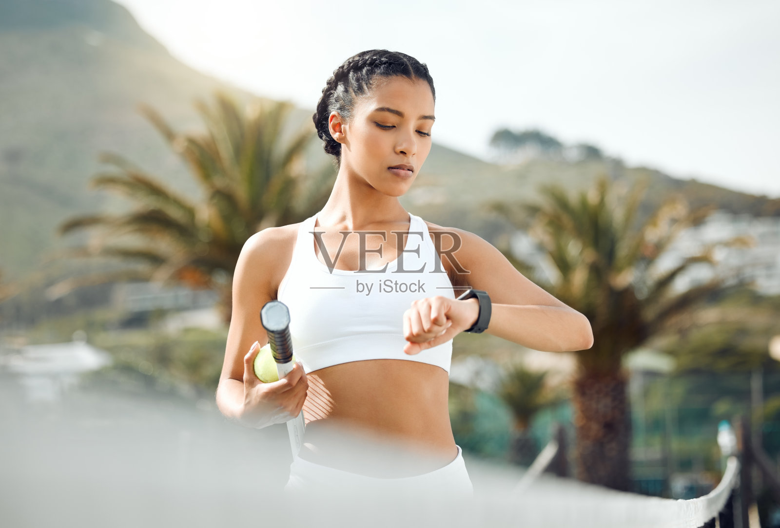 这张照片拍摄的是一个运动的年轻女子在户外打网球时查看时间照片摄影图片