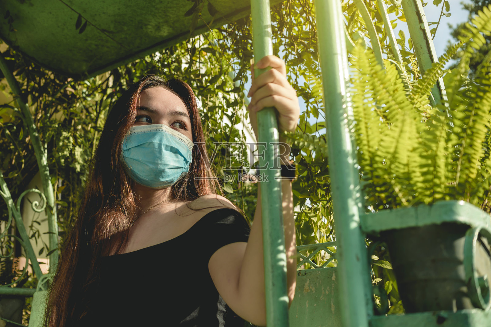 一名年轻的亚洲女性戴着口罩,茫然地看着她的右边,陷入了沉思。中性的面部表情。照片摄影图片