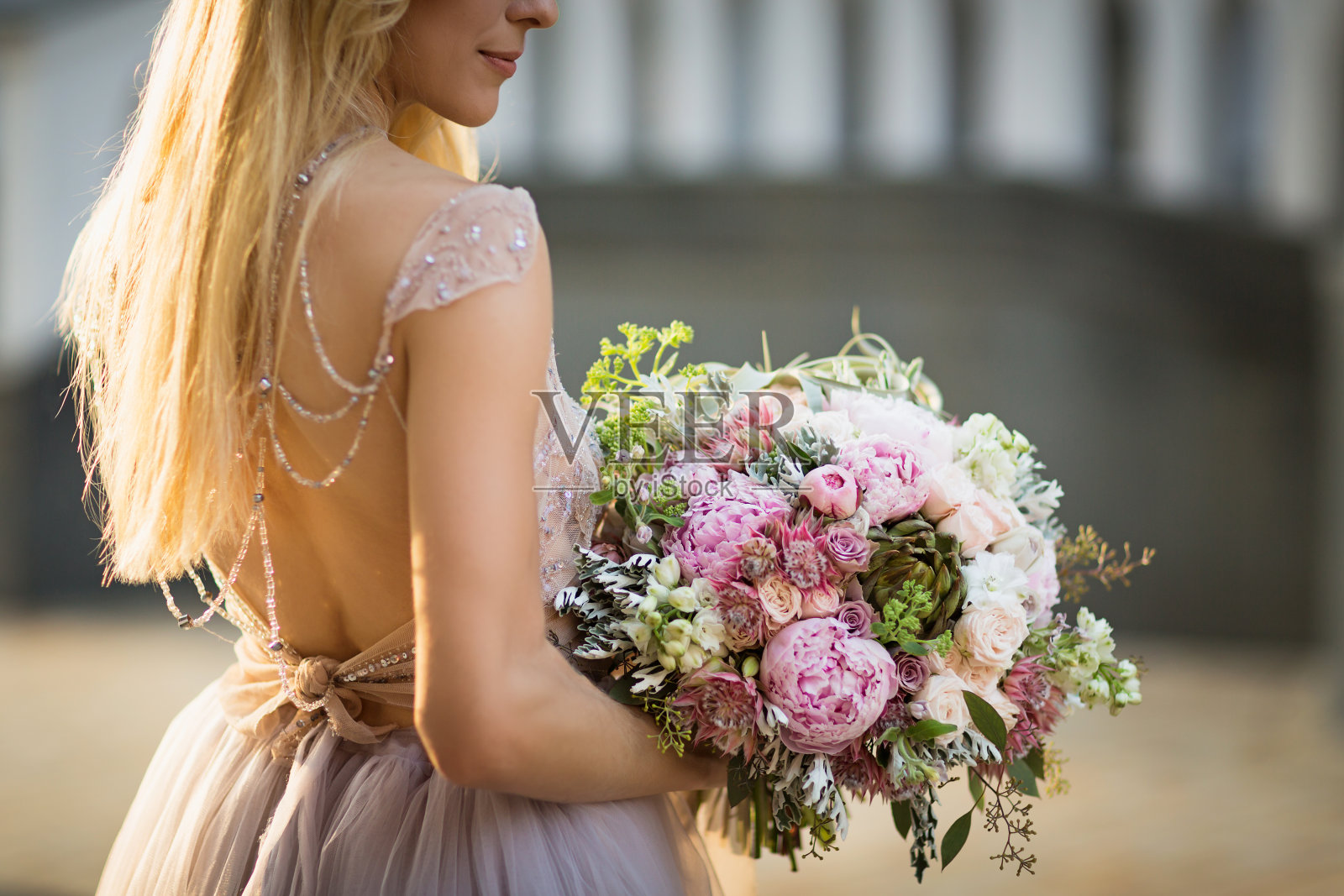 一个优雅的无法辨认的漂亮女人的肖像穿着灰色的婚纱,在街上摆姿势。新娘捧着一束柔和的鲜花和绿叶照片摄影图片