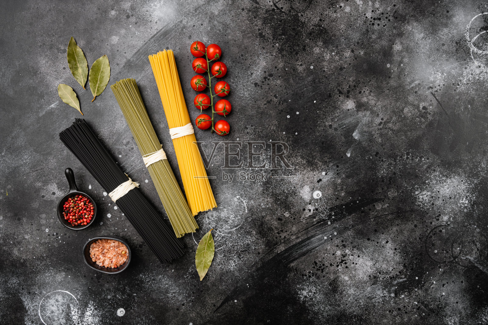 意大利面有三种颜色,黑、黄、绿,在黑、黑的石头桌子背景上,俯视图平铺,文字有复制空间照片摄影图片