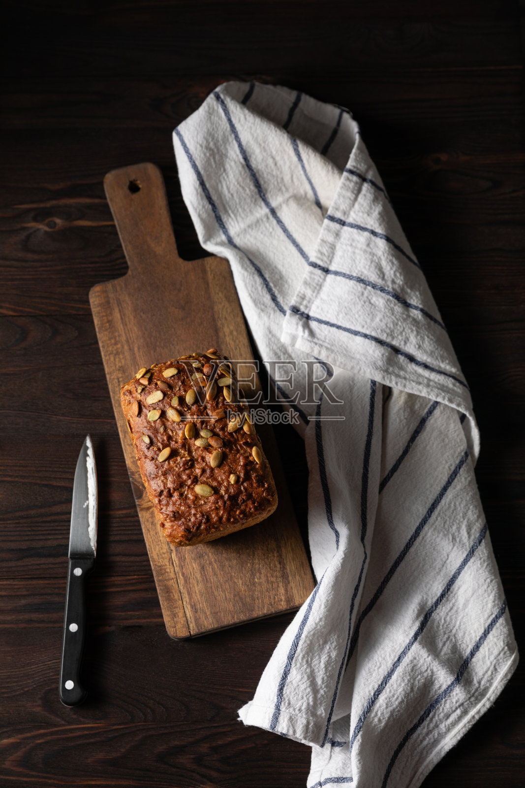 在木制背景上自制的带有南瓜籽的硬皮面包。静物的概念。黑暗的情绪。传统技术,创新面包,低碳水化合物烘焙照片摄影图片