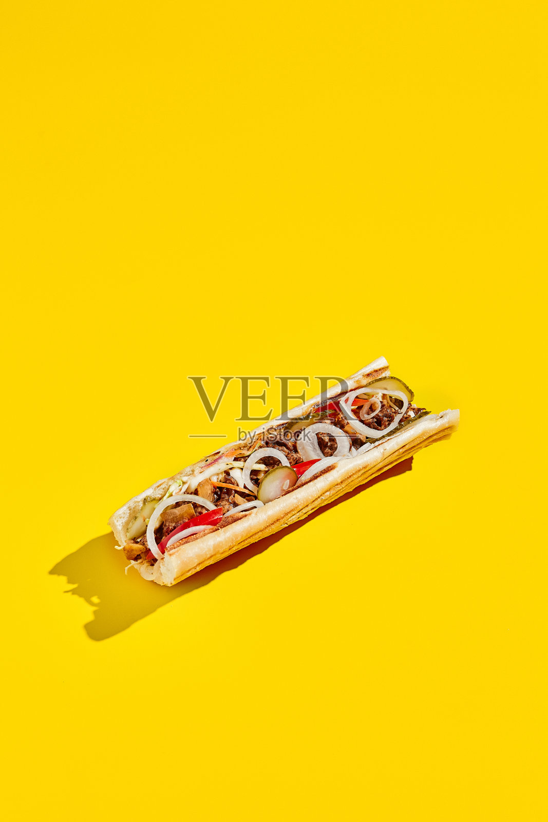 最简风格的牛肉芝士牛排配洋葱和泡菜。美国快餐在黄色的背景与阴影。费城牛排三明治的新潮概念。垃圾食品的颜色背景。照片摄影图片