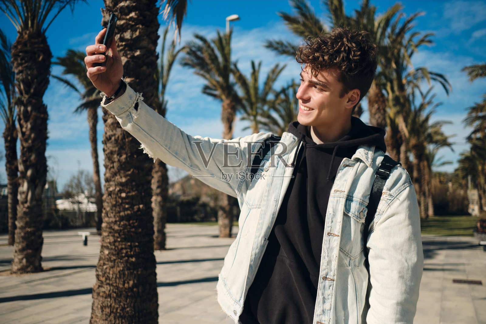 走在满是棕榈树的街道上,帅哥开心地用智能手机自拍照片摄影图片
