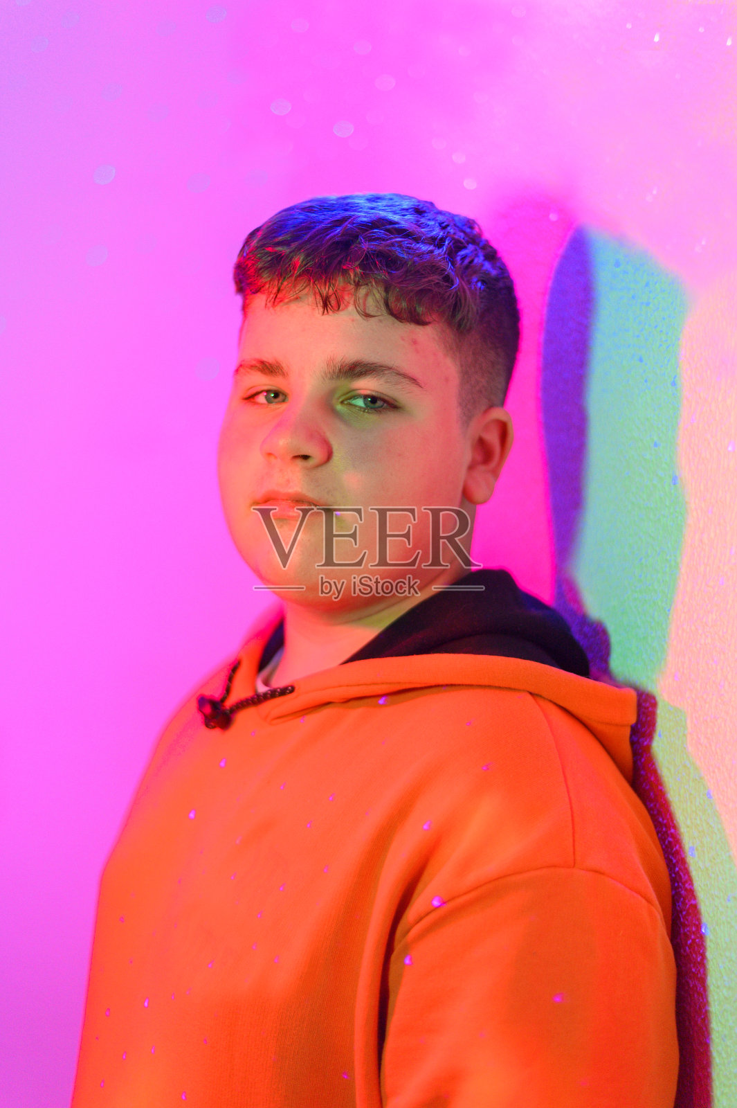 穿着运动衫的可爱少年用霓虹灯看着摄像机。照片摄影图片