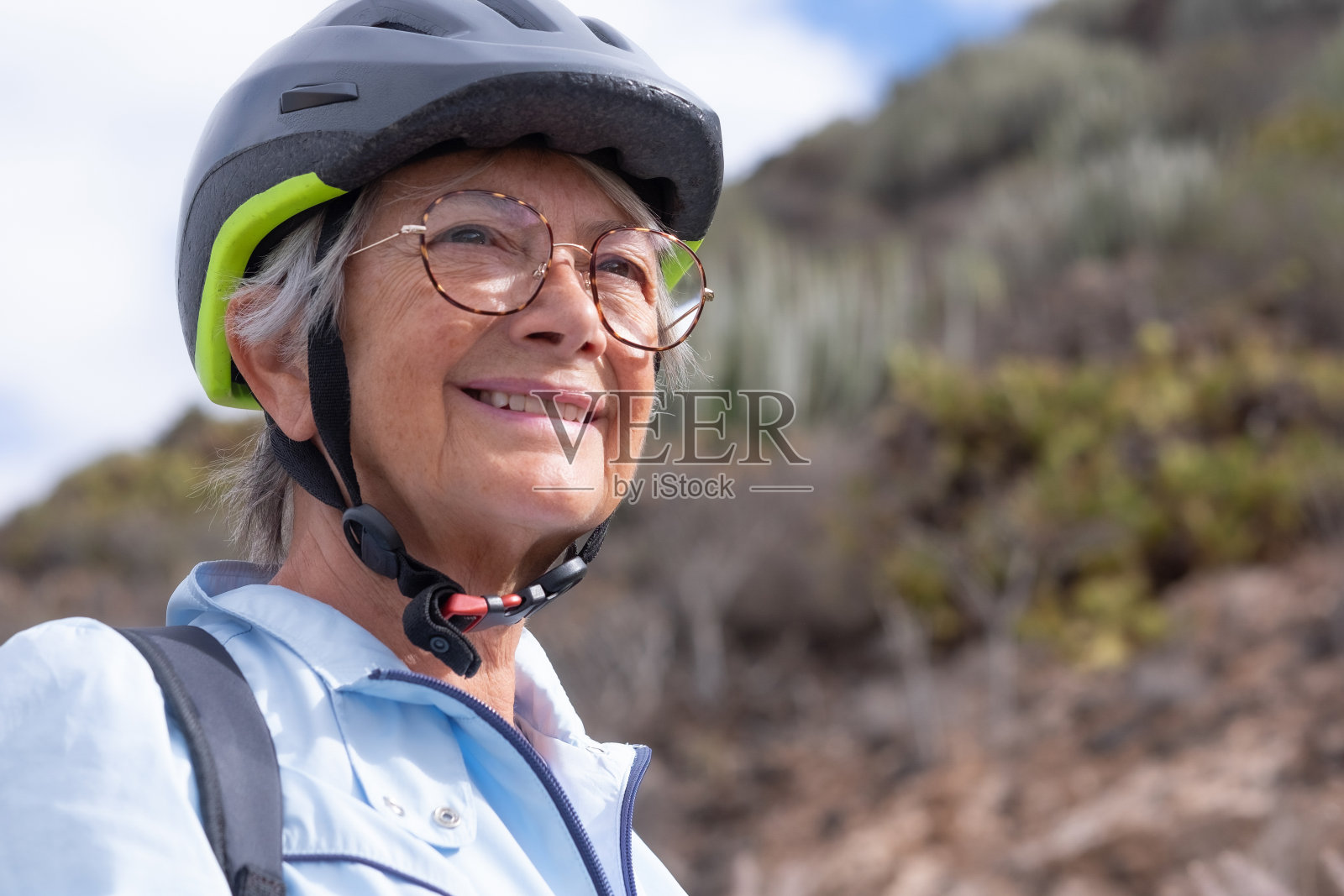 近距离的肖像活跃的成年人微笑的老年妇女戴着运动头盔和眼镜在户外远足。快乐迷人的老年女性,享受健康的生活方式和自然照片摄影图片