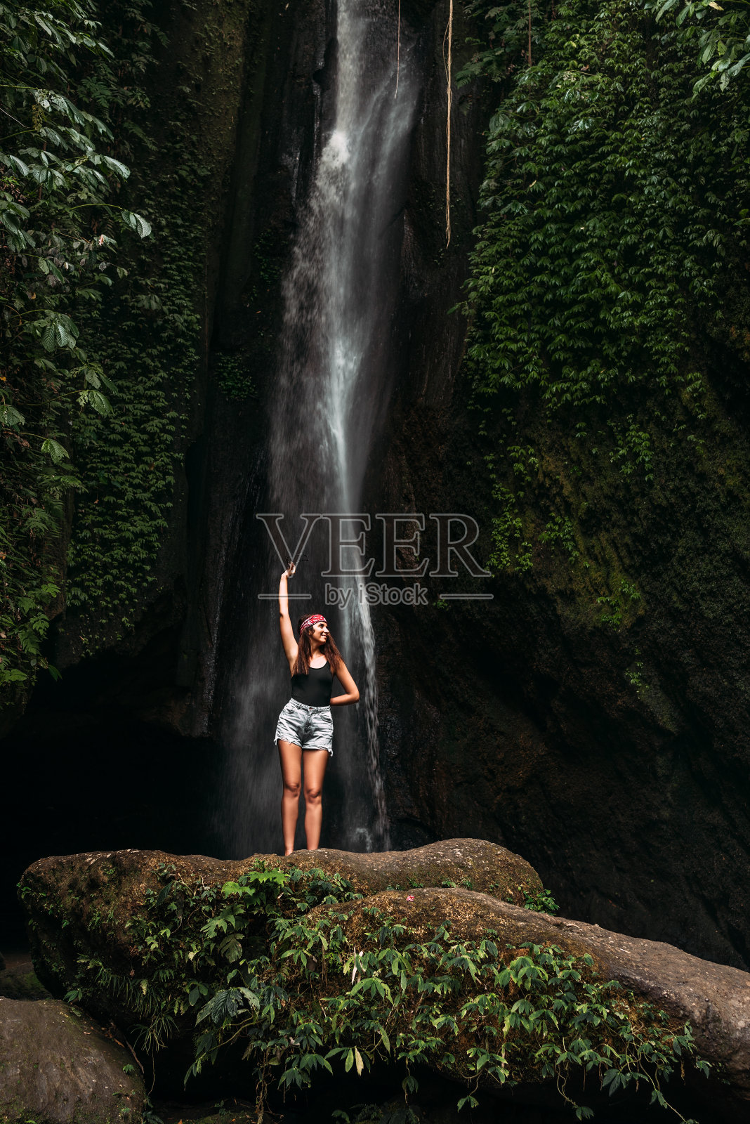 美丽的女孩在瀑布上的巴厘岛印度尼西亚。瀑布上的性感女人。年轻美丽的女孩在比基尼在瀑布洗澡。美丽的女人在瀑布前摆姿势。照片摄影图片