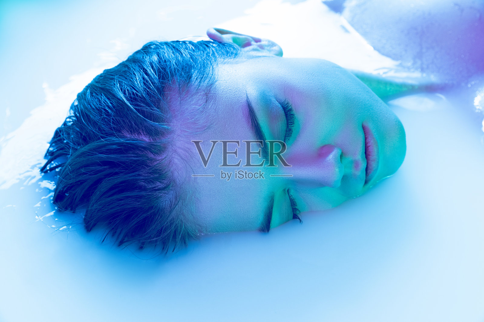 女性的特写脸,年轻美丽的女孩在牛奶浴与柔和的发光在蓝绿色霓虹灯。美容、时尚、风格、护肤理念照片摄影图片