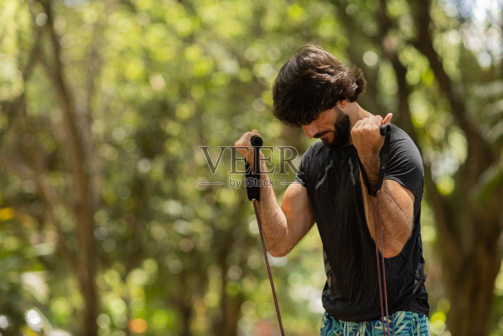 一个强壮的男人在户外的公园里用橡皮筋锻炼。男性运动员在锻炼时使用额外的运动器材。高质量的照片照片摄影图片