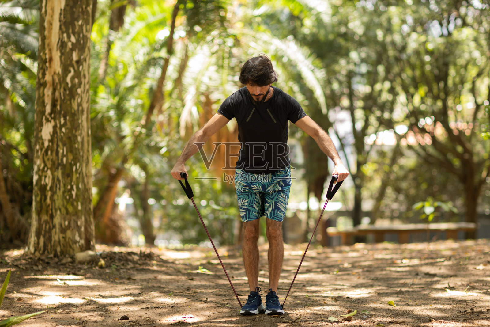 一个强壮的男人在户外的公园里用橡皮筋锻炼。男性运动员在锻炼时使用额外的运动器材。高质量的照片照片摄影图片