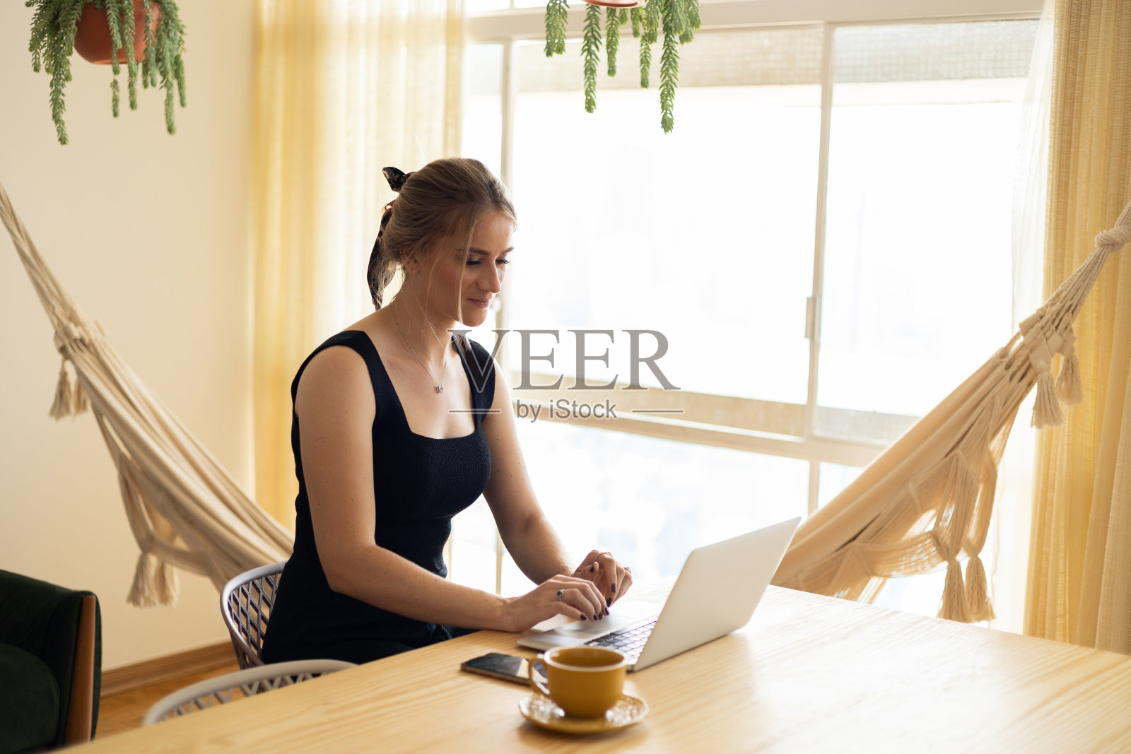 年轻的商人在家里的厨房里工作,笔记本电脑和厨房木桌上的文件。家庭办公室的概念。照片摄影图片