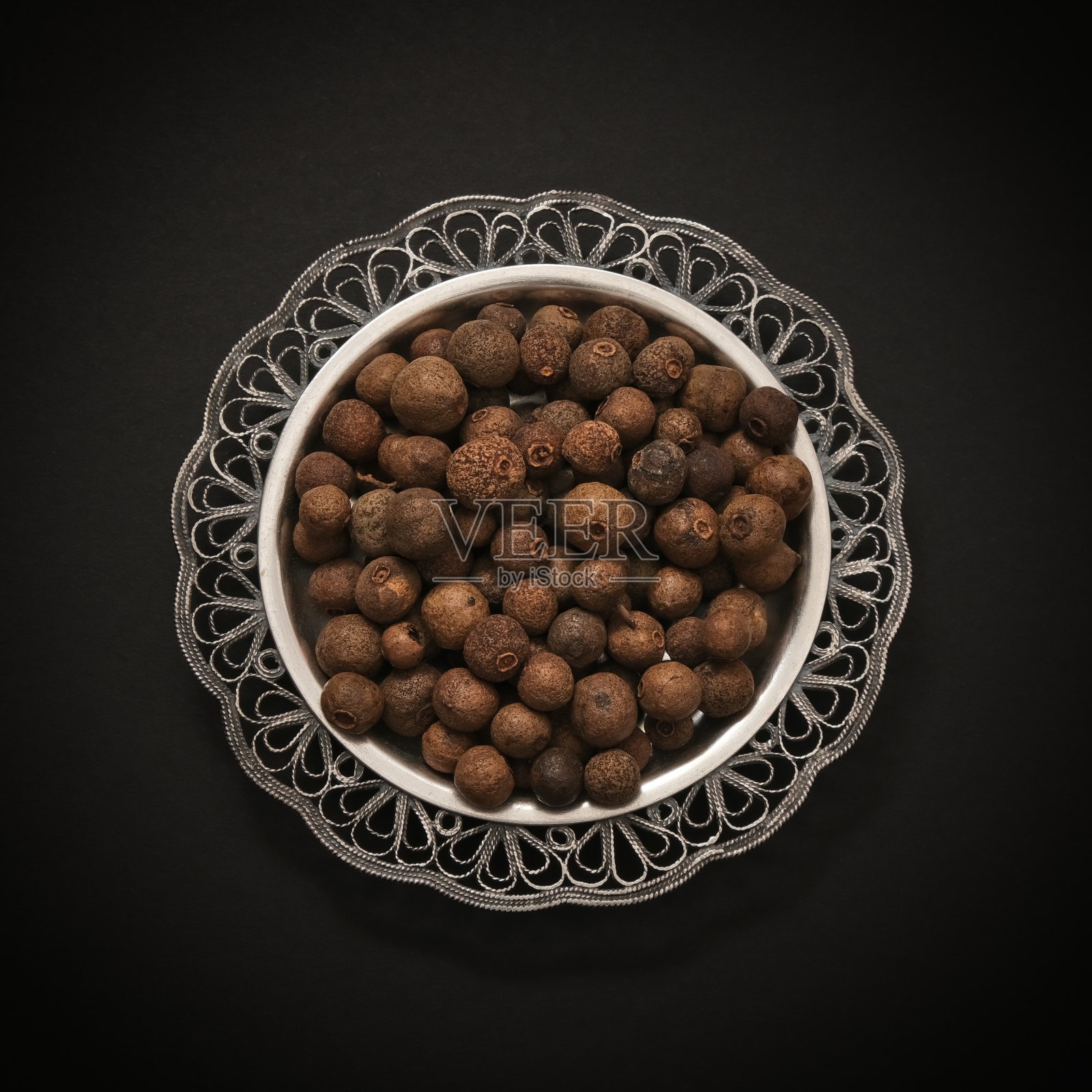 黑色背景的复古银碟中,一堆干燥的成熟的胡椒浆果多香果豌豆特写。有机犹太洁食手工挑选的牙买加多香果。异国情调的Pimento胡椒照片摄影图片