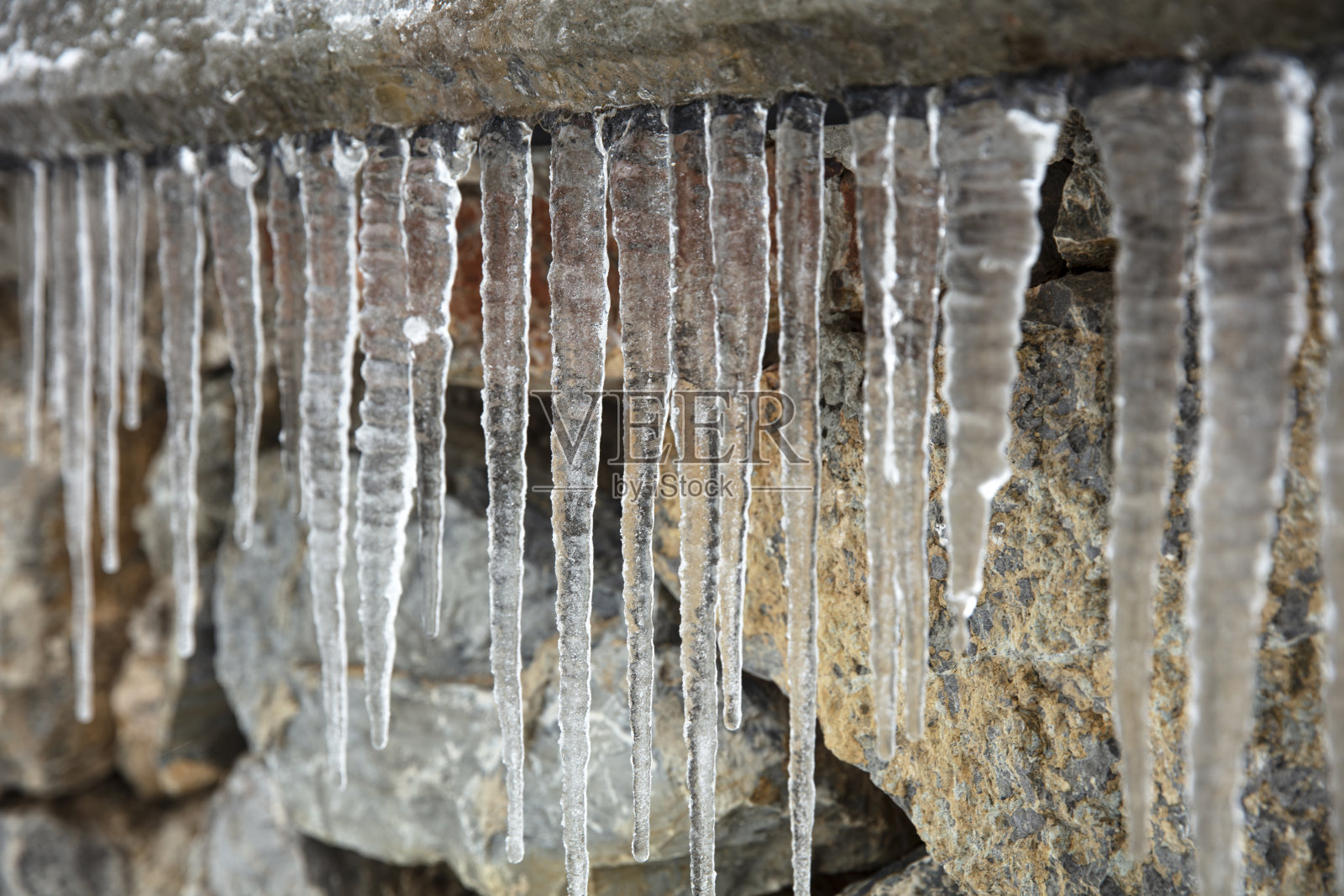 石墙背景上的大组冰柱照片摄影图片
