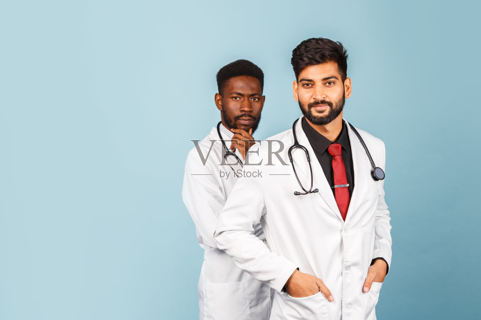 一名身穿白大褂的医务人员在蓝色背景下手持听诊器与一位年轻医生交谈的特写照片摄影图片