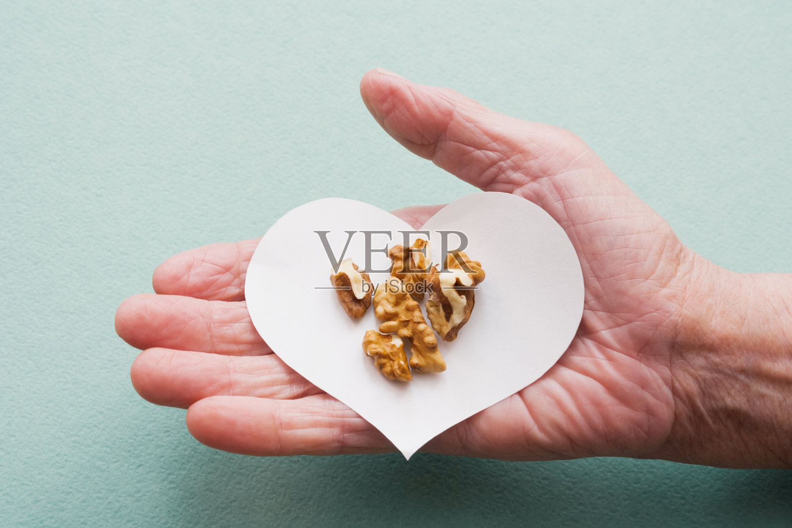 一位老妇人的手握着一颗心和核桃照片摄影图片