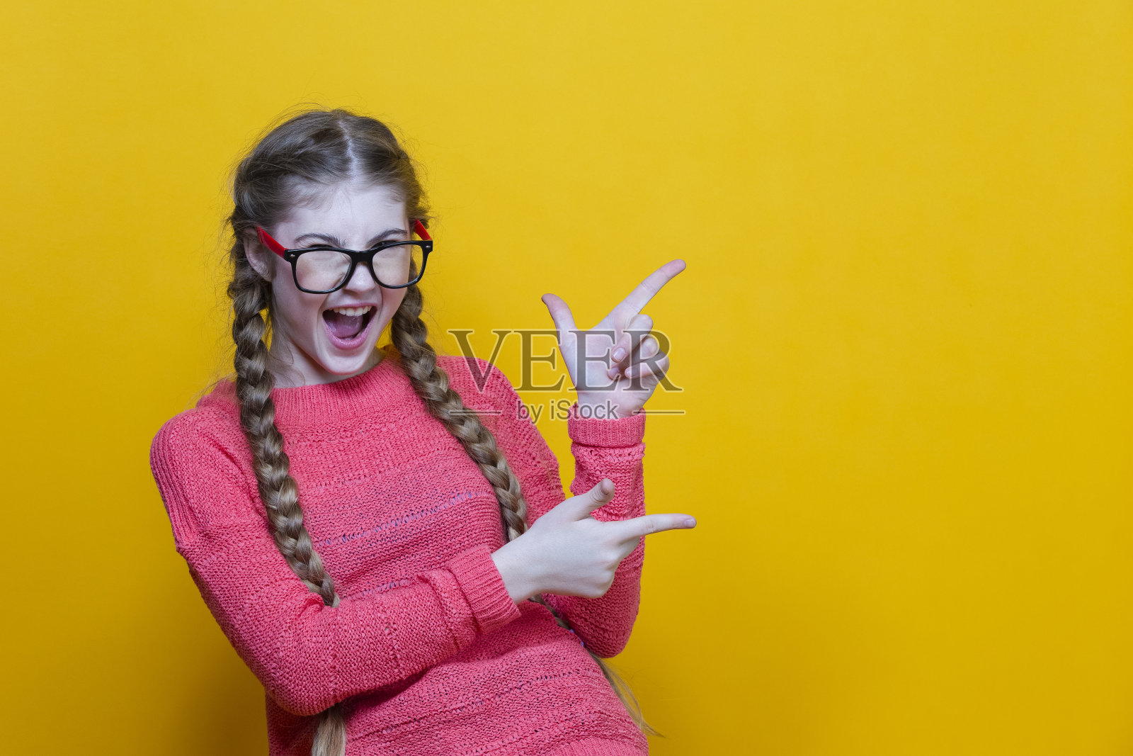 白种人女孩的肖像,穿着珊瑚编织的毛衣,戴着眼镜,指着黄色的一边照片摄影图片