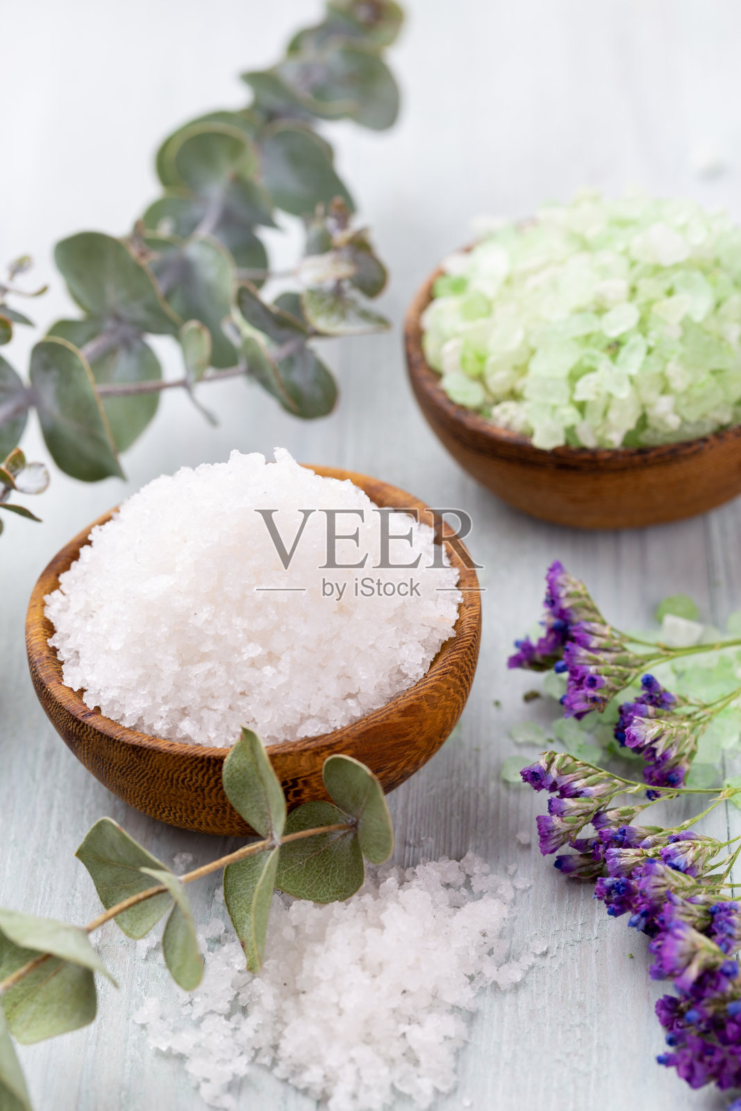 海盐在碗里,香精油在瓶子里,健康和花在灰色纹理背景和花在复古的木质背景上。有选择性的重点。照片摄影图片