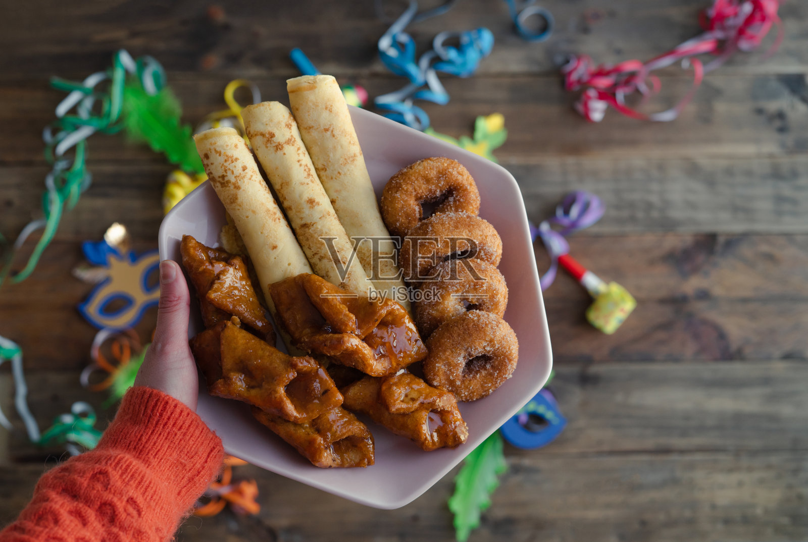 女人的手捧着一盘嘉年华糖果。木制背景与狂欢节装饰。照片摄影图片