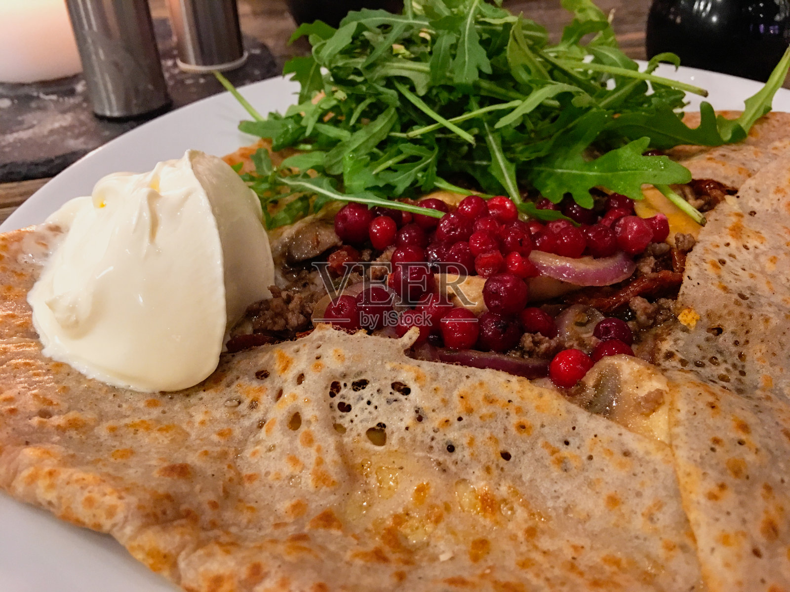 一种用炸肉、蘑菇、越橘、芝麻沙拉和鲜奶油填充的可丽饼或薄饼照片摄影图片