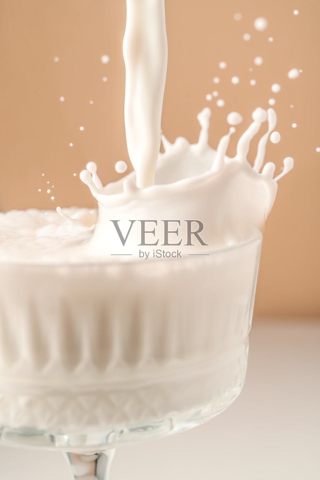 牛奶倒入一个漂亮的水晶玻璃杯,溅得到处都是。照片摄影图片