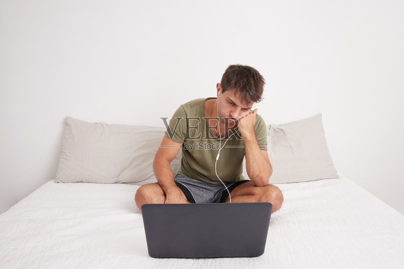 一个年轻人无聊地坐在床上用笔记本电脑开视频会议照片摄影图片