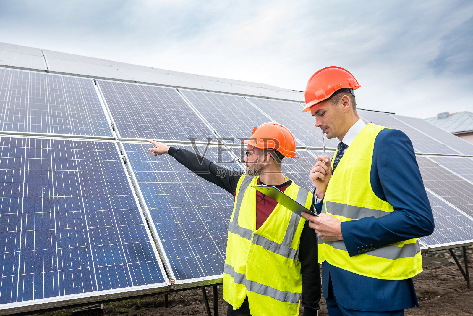 身穿制服、头戴头盔的商人告诉工人安装太阳能电池板的计划。照片摄影图片