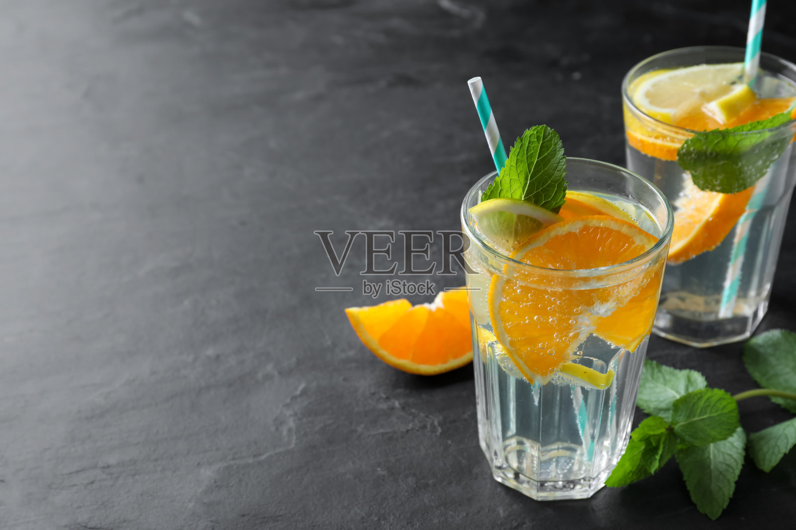 在黑色的桌子上放着美味的橙汁柠檬水,配上苏打水和薄荷,留出文字空间。新鲜的夏季鸡尾酒照片摄影图片
