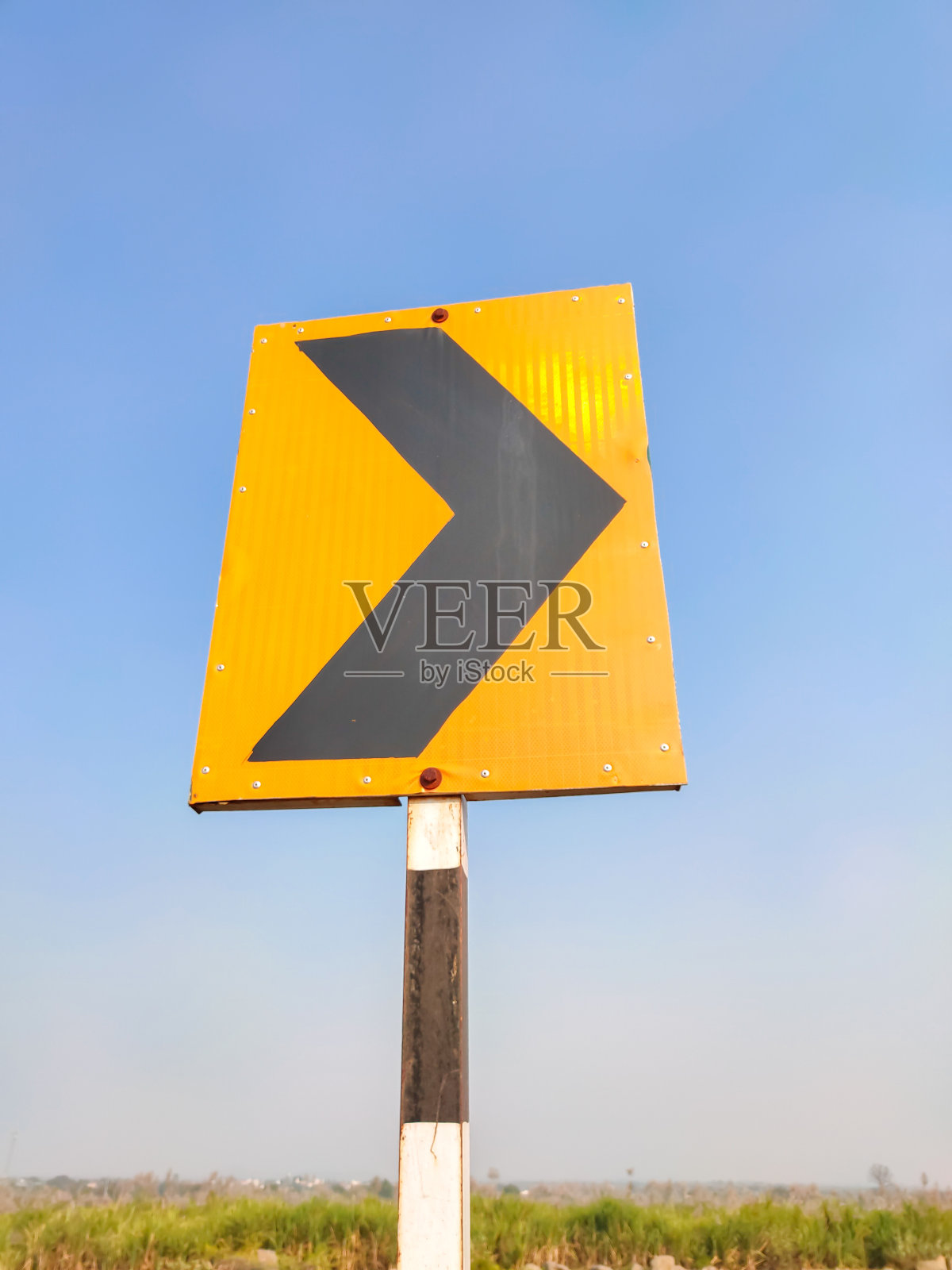 黑色箭头右指的标志,警告有蓝色天空背景的弯曲道路照片摄影图片