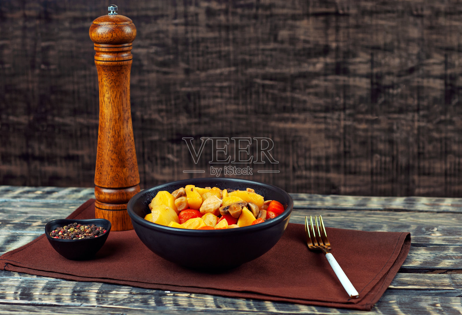 在黑色的碗里煮土豆和肉。土豆配蘑菇和胡萝卜。煮蘑菇和土豆鸡肉。黑色的木桌上放着食物。复制空间和土豆附近的自由空间。照片摄影图片