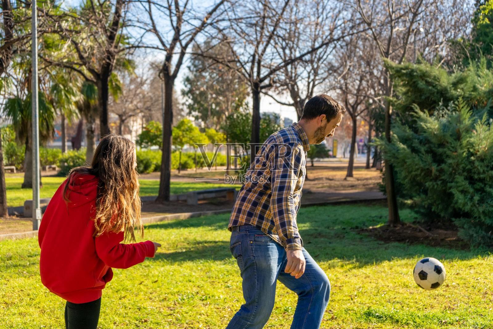 在一个阳光明媚的冬日,父亲带着一个不到十岁的女儿在一个美丽的公园的草地上踢足球。运动与健康生活理念。照片摄影图片