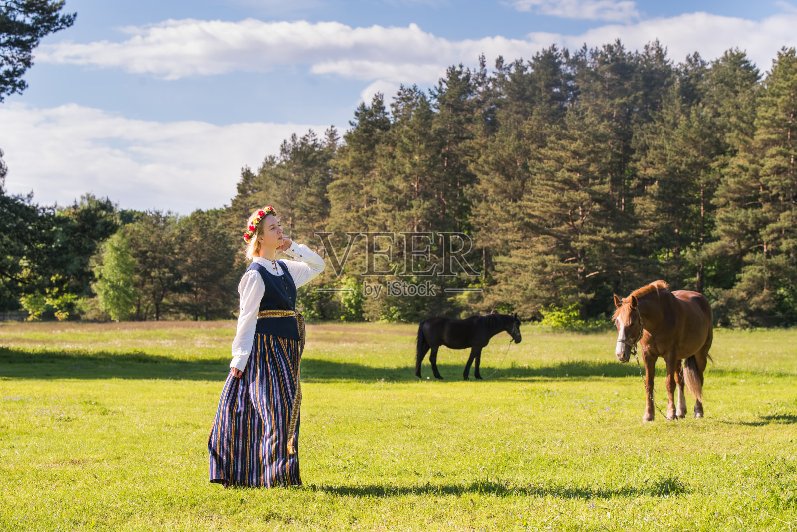 拉脱维亚妇女穿着传统服装与马在自然中摆姿势。照片摄影图片
