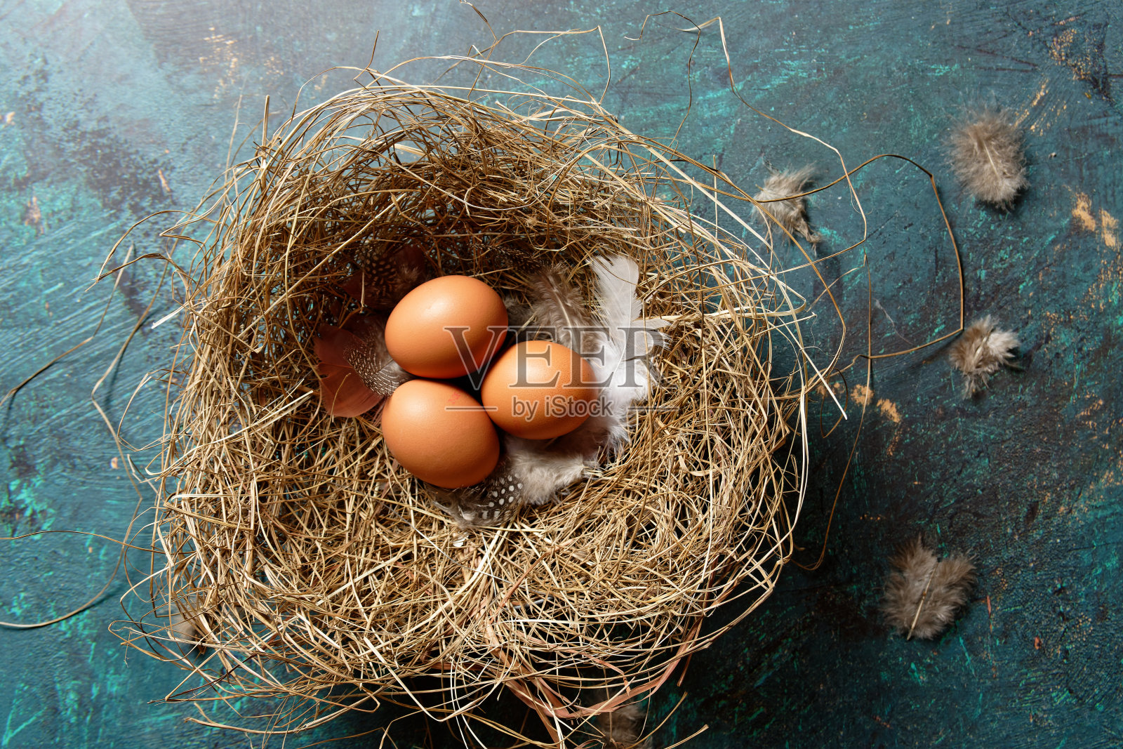 三个棕色的生鸡蛋在干草做的窝里。照片摄影图片