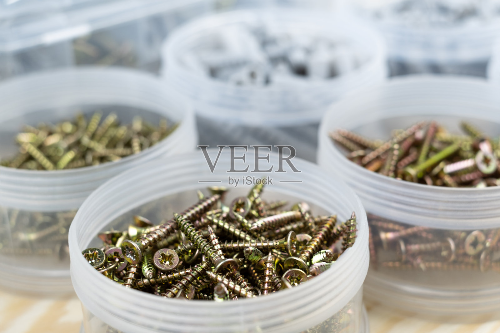 各种尺寸的螺钉和销钉,装在透明塑料盒容器内,放在木盒上。近看,俯视图。照片摄影图片