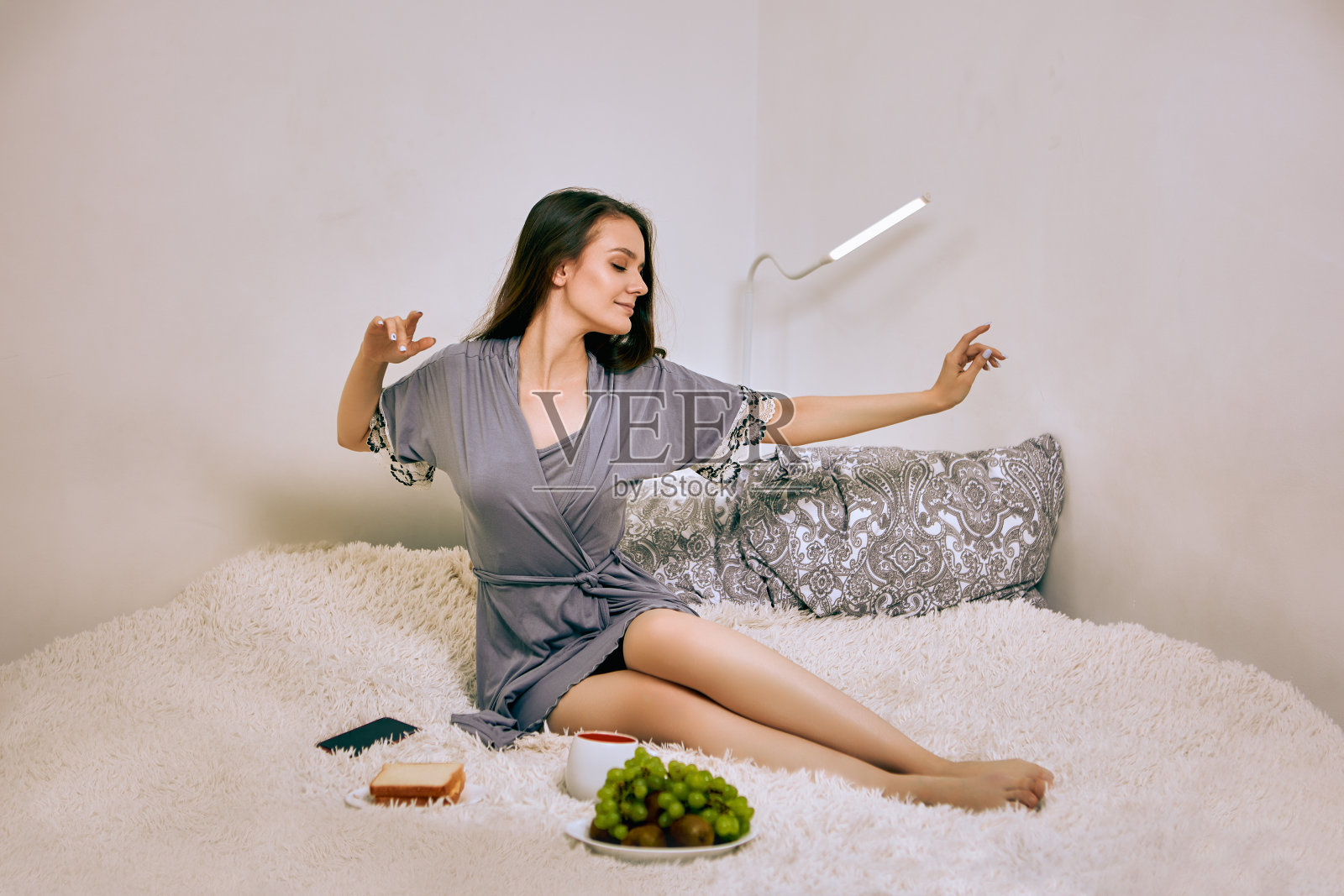 室内,穿着睡衣的苗条女子在床上吃早餐。照片摄影图片