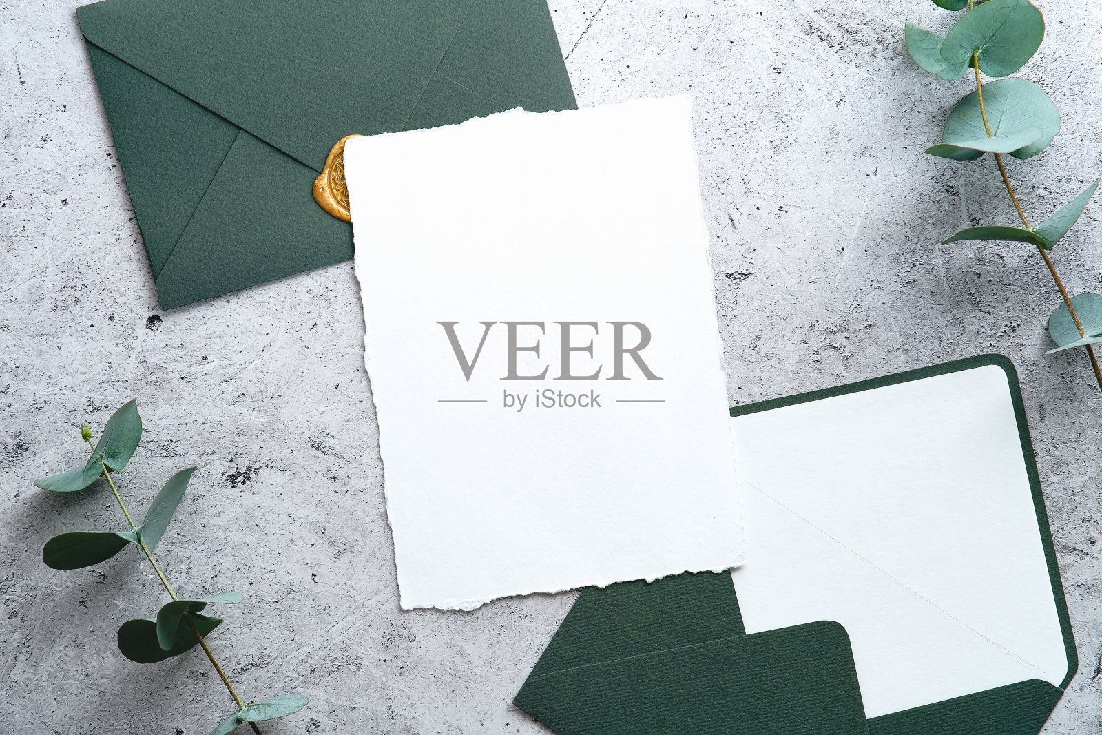 在石头桌子上,有绿色信封和桉树树枝的婚礼请柬模型。俯视图,平躺,头顶。照片摄影图片