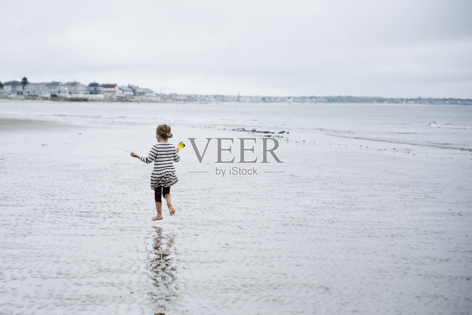 顽皮的小女孩在寒冷和阴天的海滩上。照片摄影图片