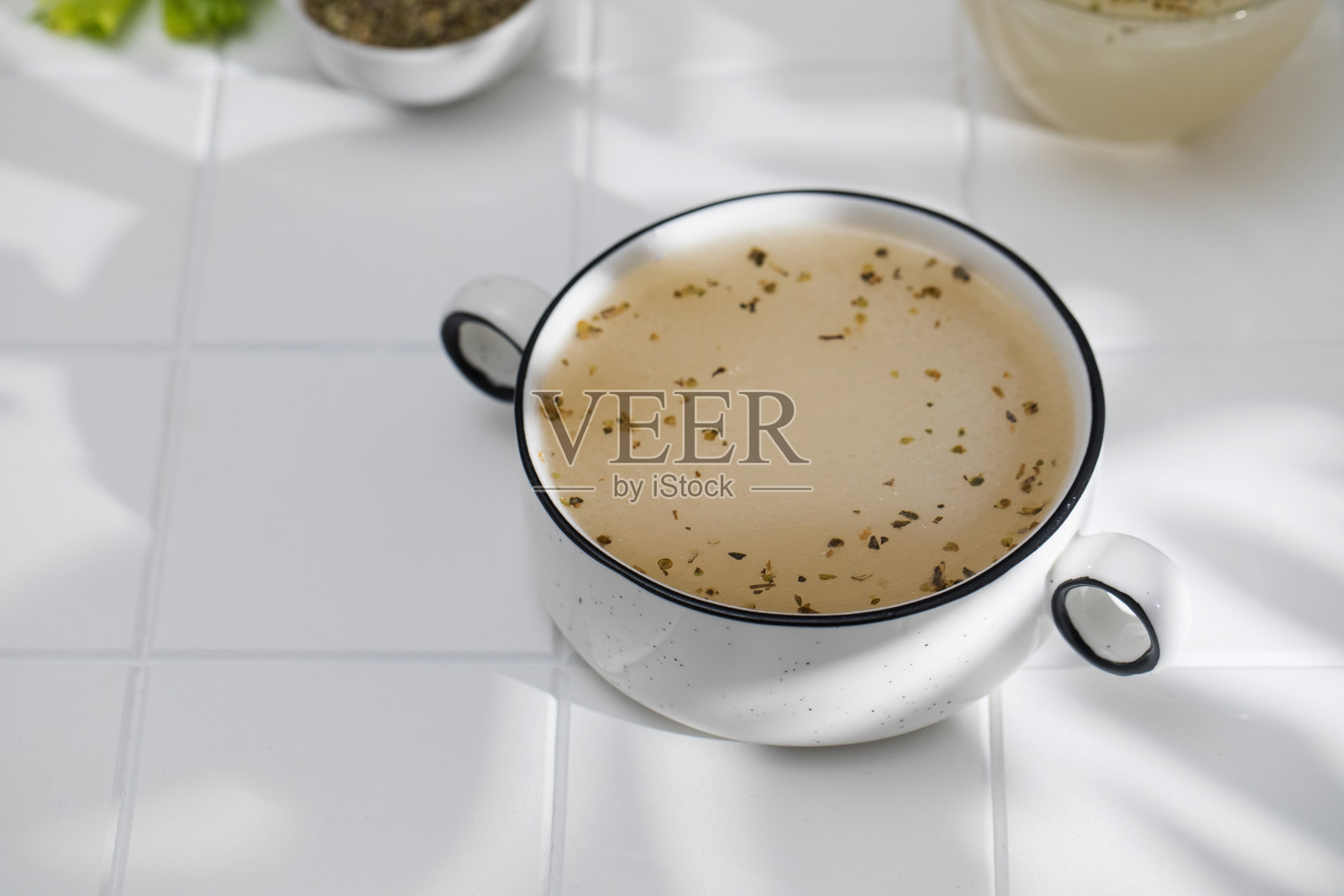 健康的骨汤与香料碗上白色瓷砖阴影图案。生酮饮食和旧石器饮食的概念。照片摄影图片