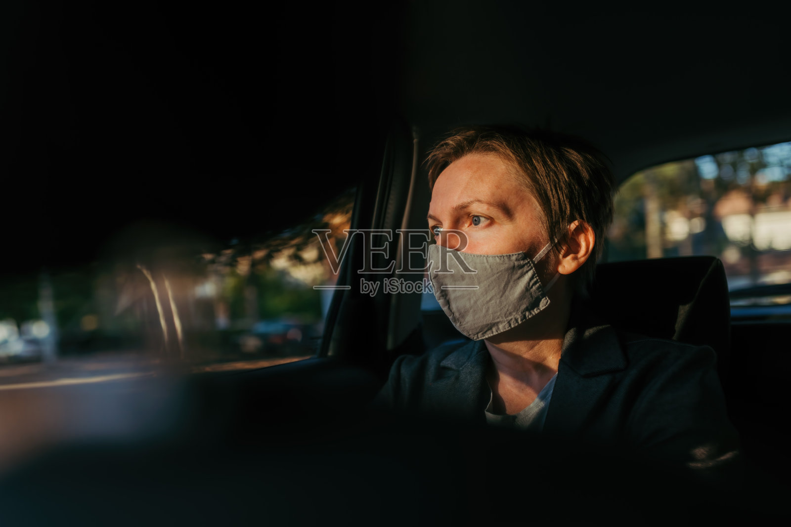 忧心忡忡的女商人,带着防护面罩,在车里等着,看着窗外照片摄影图片