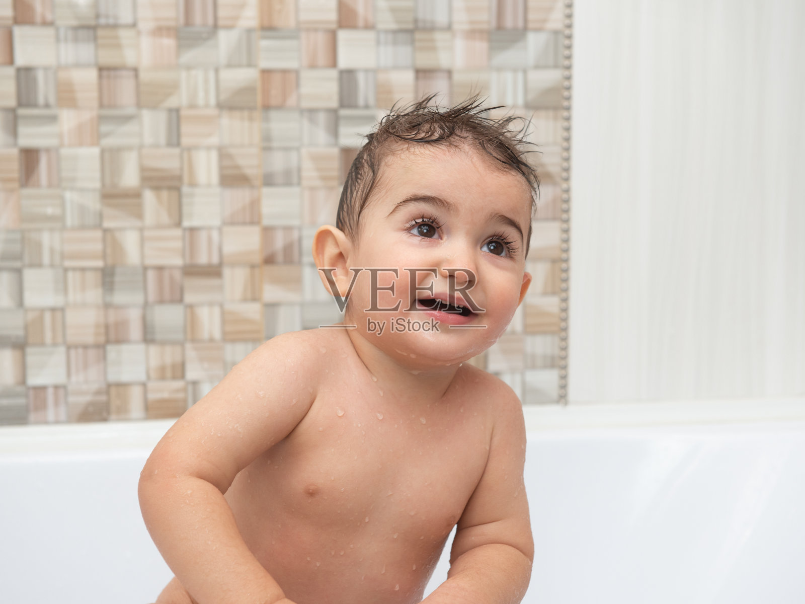 在浴室里洗澡的孩子的肖像。棕色的眼睛睁得大大的。照片摄影图片