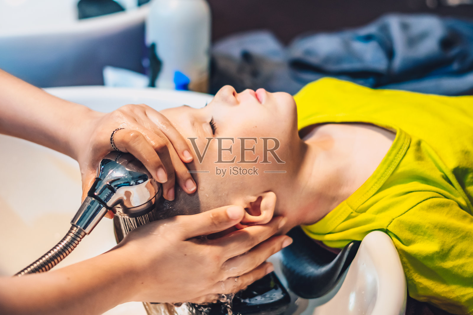 湿头金发小男孩斜靠在水槽上。女性女性的手。洗发按摩取香波泡沫,淋浴喷水。美容院。理发师的工作。孩子喜欢理发店。发型孩子端照片摄影图片