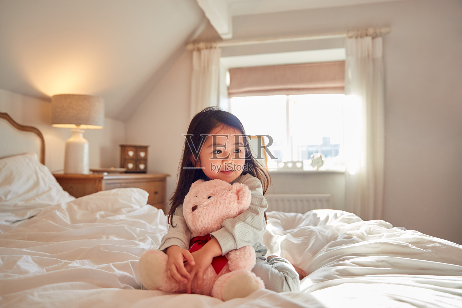 小女孩坐在床上穿着睡衣在家里抱着软玩具照片摄影图片