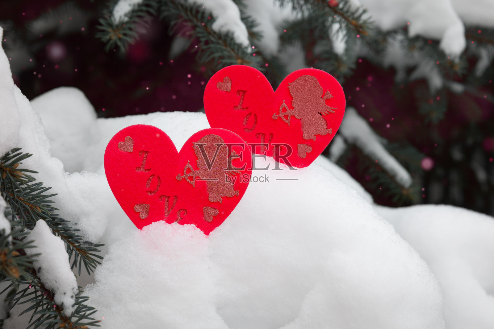 两颗红心和天使在雪松的树枝上,为圣瓦伦丁节。照片摄影图片