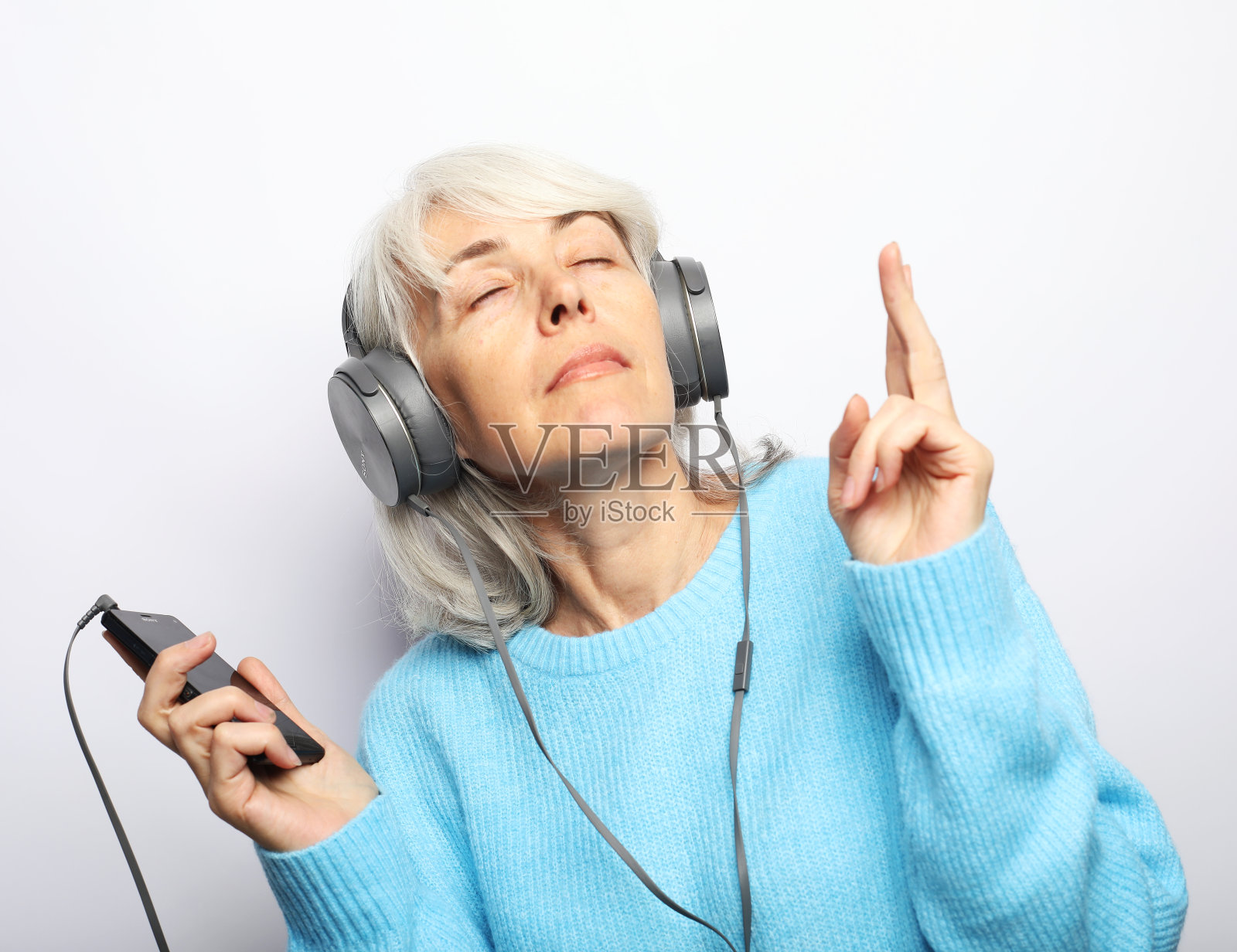 一位快乐的老妇人,戴着耳机在白色背景上听音乐照片摄影图片