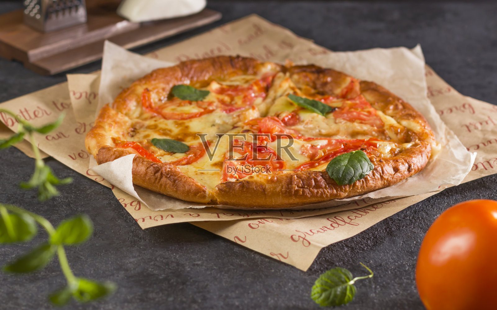 美味新鲜的自制快餐。传统的玛格丽塔披萨,番茄,罗勒和马苏里拉奶酪特写,羊皮纸在黑暗的背景上照片摄影图片