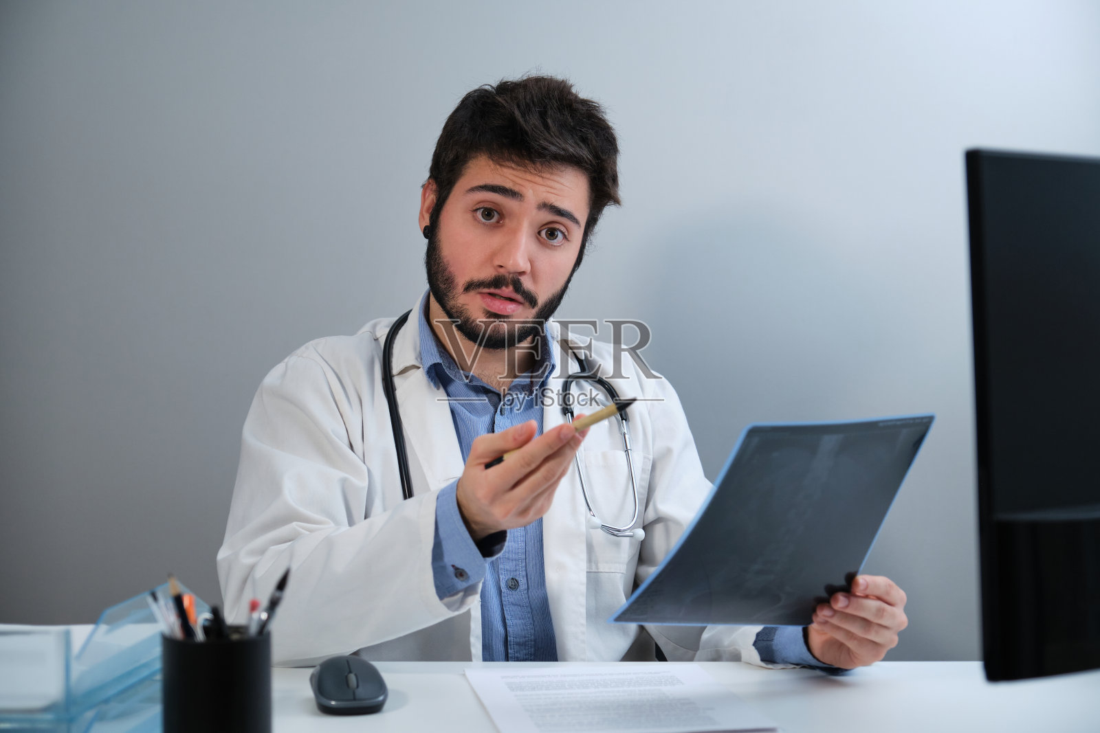 年轻的医生看着摄像机说着骨盆的x光片。照片摄影图片