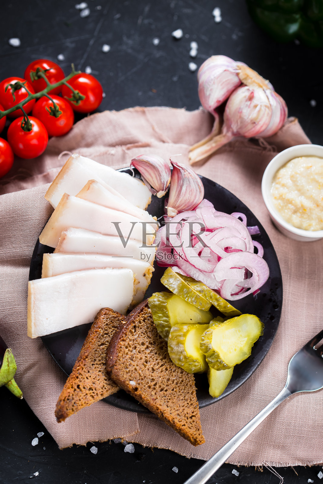 在一盘冷开胃酒,新鲜培根片,煮土豆,洋葱圈和黑面包,樱桃番茄,刀具上一个黑色孤立的背景,顶部照片摄影图片
