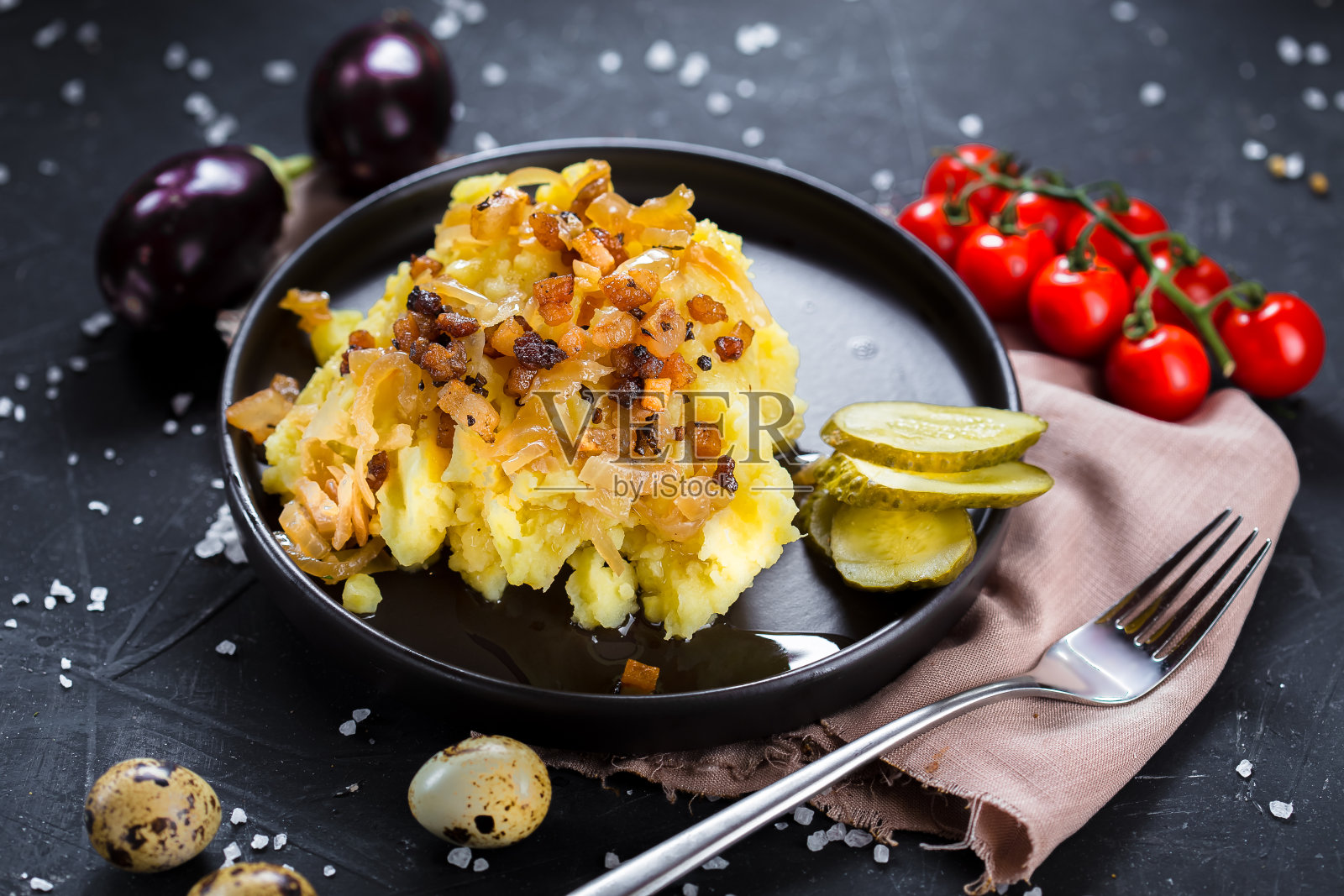 在一个盘子上煮土豆,炸洋葱和培根,洋葱圈和黑面包,樱桃番茄,刀具在一个黑色孤立的背景,顶部照片摄影图片