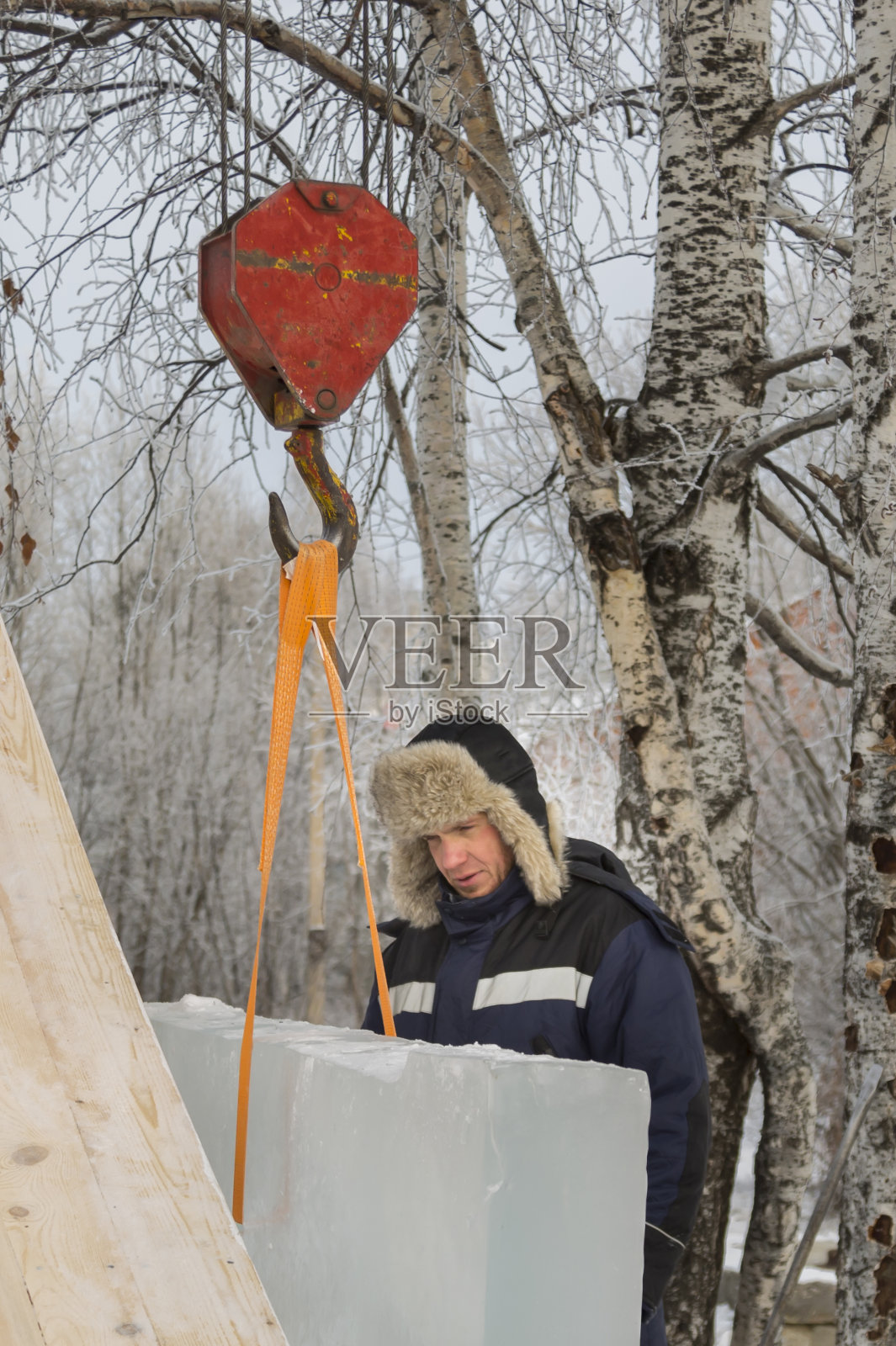 图为一名工人站在卡车起重机的吊钩旁照片摄影图片