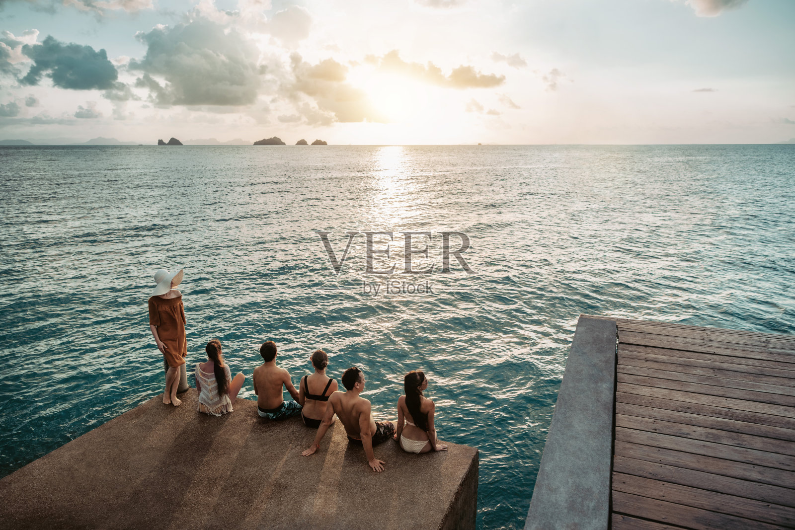 一群年轻朋友在日落时分坐在码头上照片摄影图片