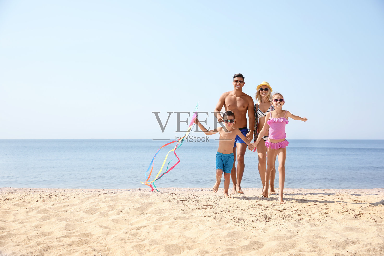 阳光明媚的日子里,幸福的一家人带着风筝在海滩上玩耍照片摄影图片